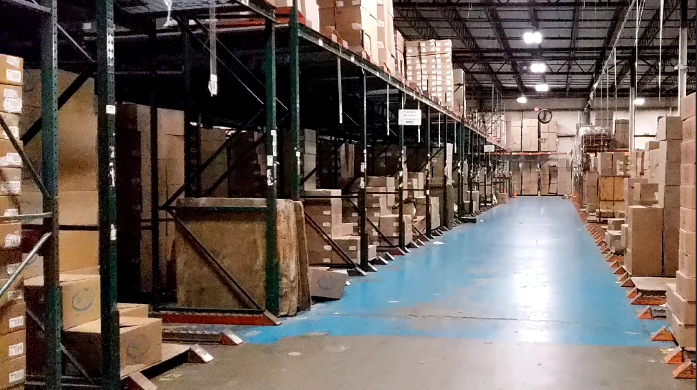 A long warehouse aisle lined with pallet racking on both sides, with a painted walking lane down the center.