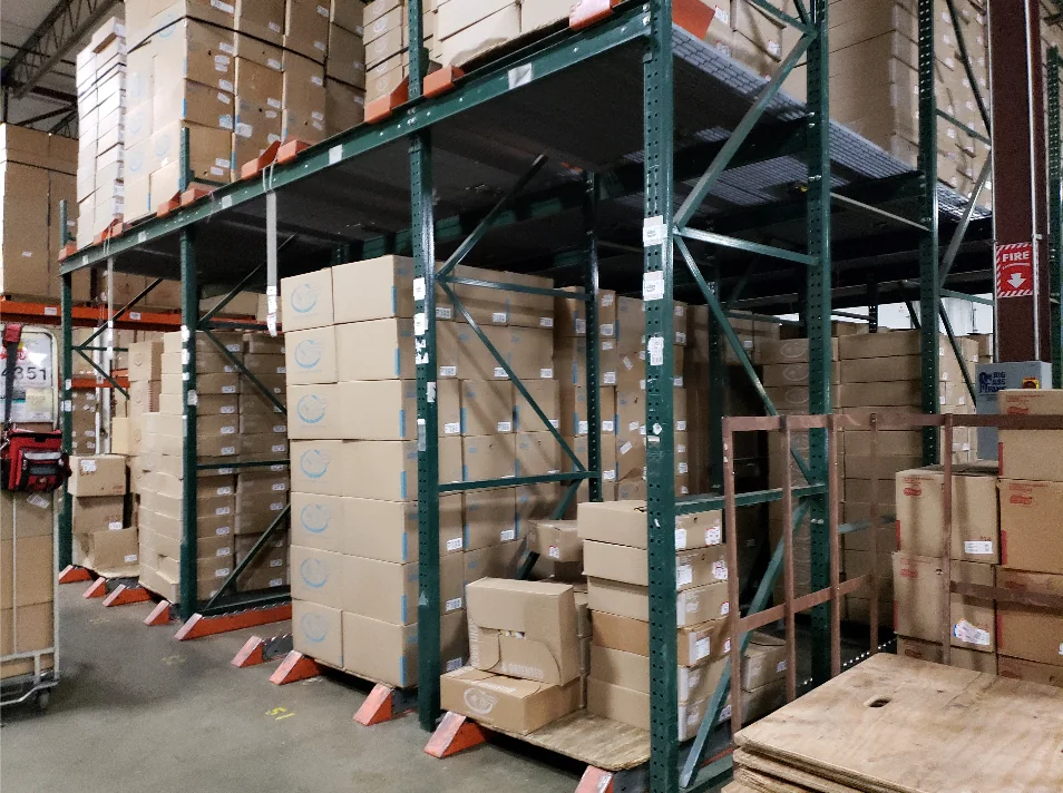 A racking bay stacked with identical cardboard cartons, with a fire-equipment sign the clearest marking in view.